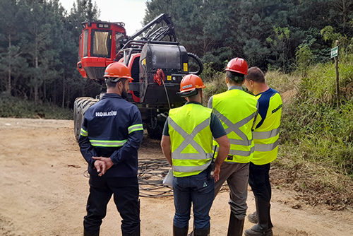 Alunos da Komatsu School em aula prática ao lado de harvester no campo